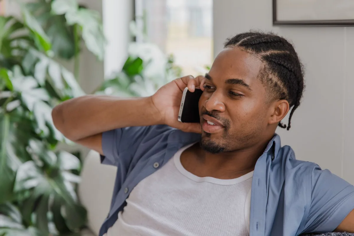 A man sitting in his living room, phone to his ear, mid-conversation