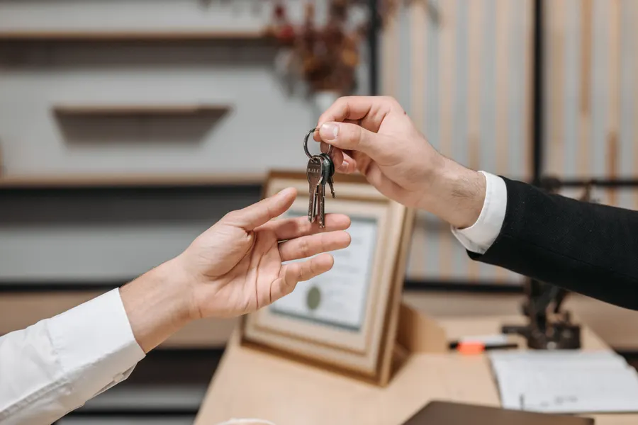 One person hands a set of keys across a desk to another person's open hand