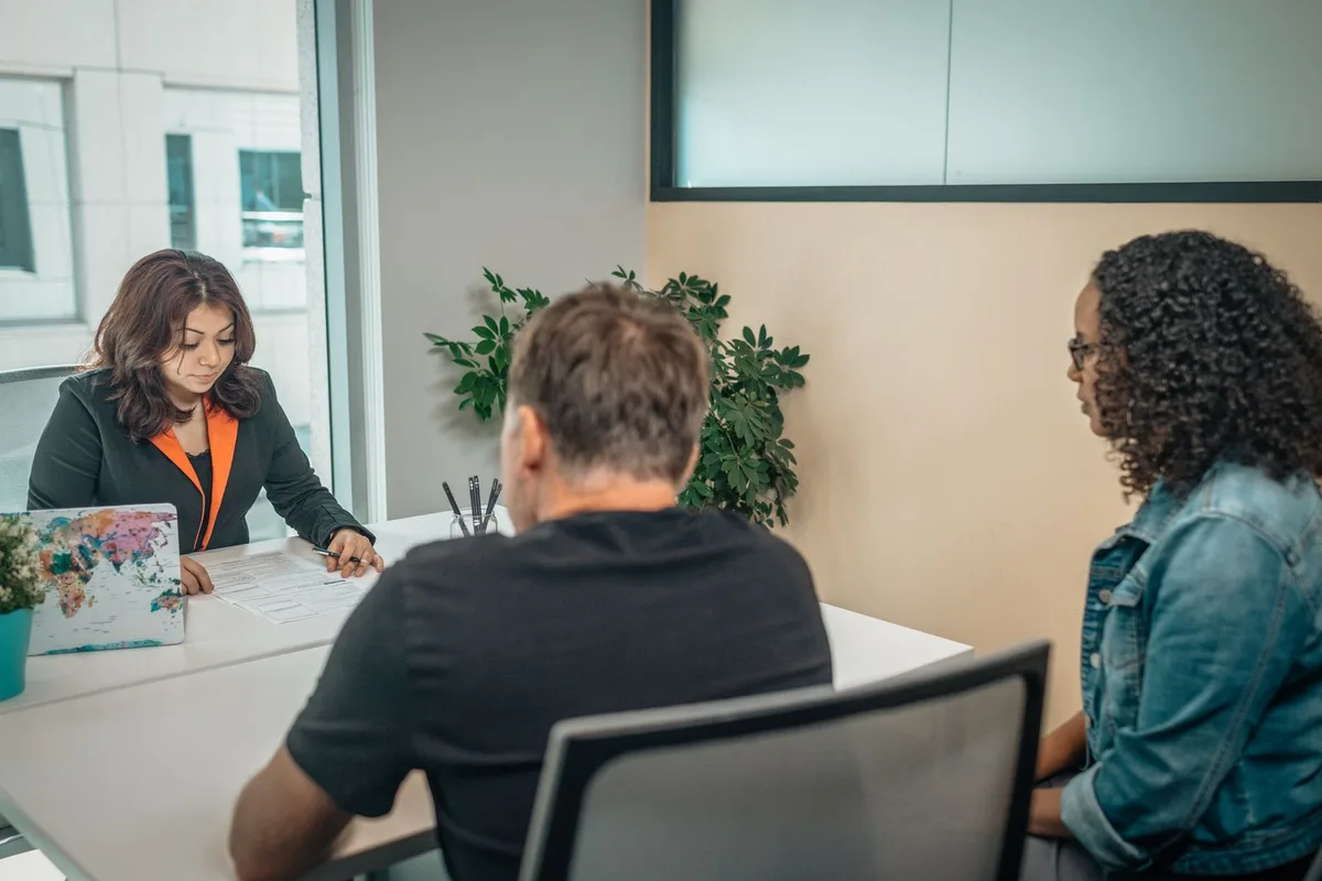 A staff member going through an application form with two visitors across a desk at a community agency office