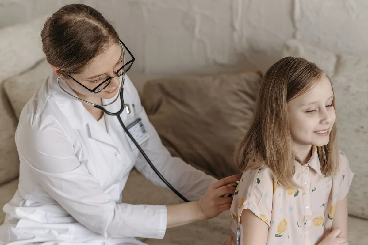 A doctor listens to a smiling girl's heartbeat with a stethoscope during a check-up