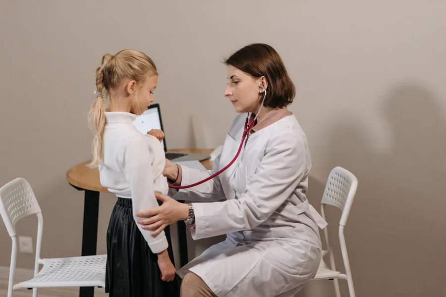 A pediatrician using a stethoscope to examine a young girl in a clinic office