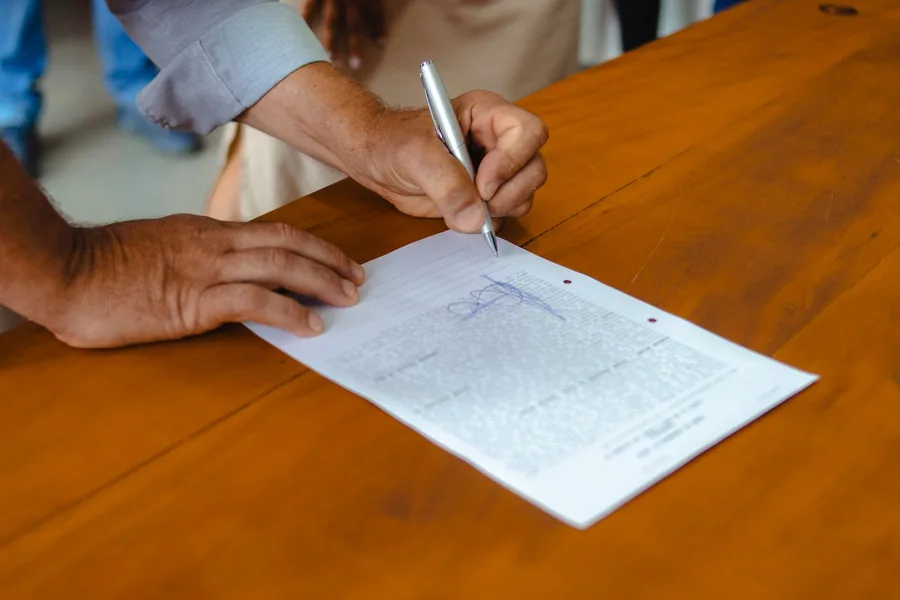 An adult's hands signing a printed form on a wooden table