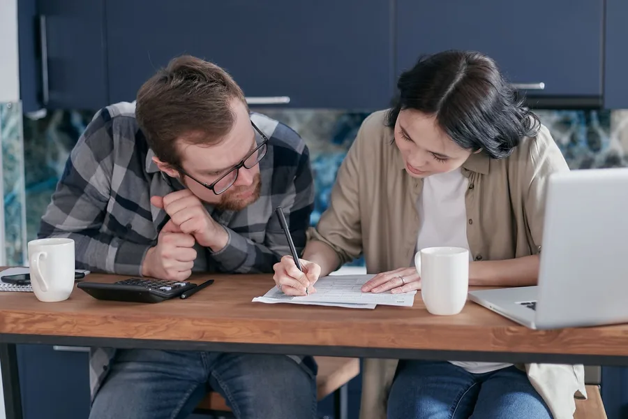 A couple at their kitchen table going over paperwork together with a calculator and laptop