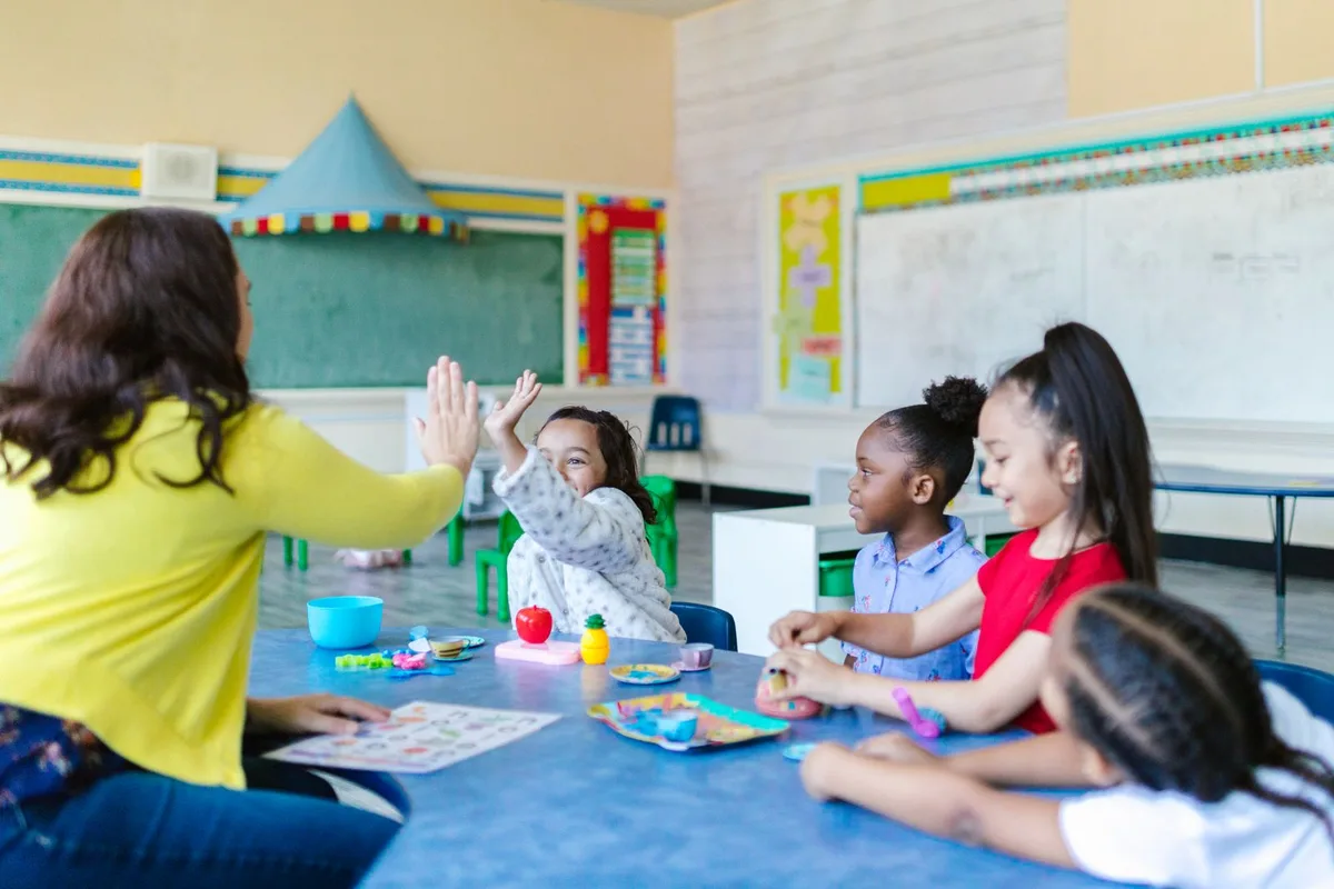 A teacher and young children playing a matching game together at a table in a bright daycare classroom
