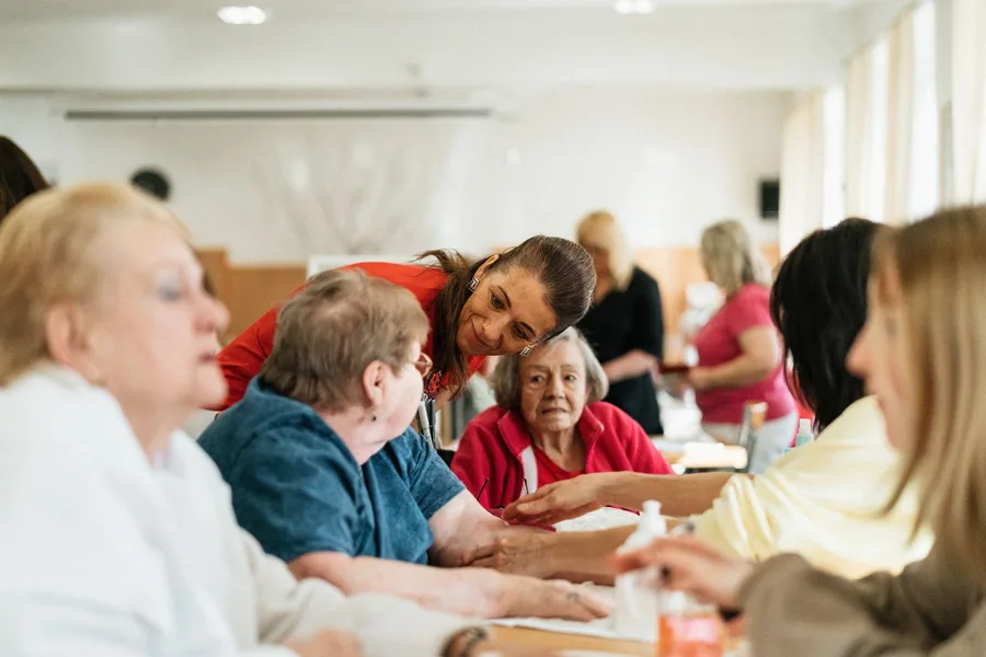 Staff at a community center lean in to talk with older adults seated around a table