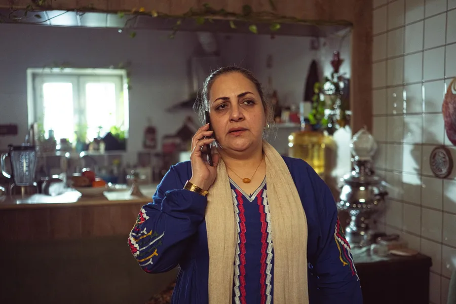 A woman stands in her kitchen at home, phone to her ear, mid-conversation