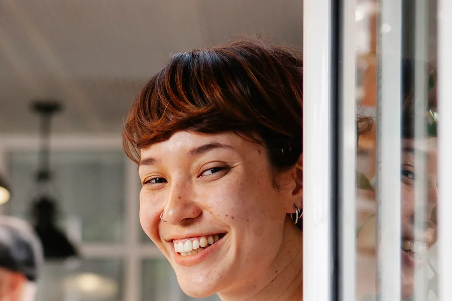 A smiling young cafe worker standing at the door of the shop