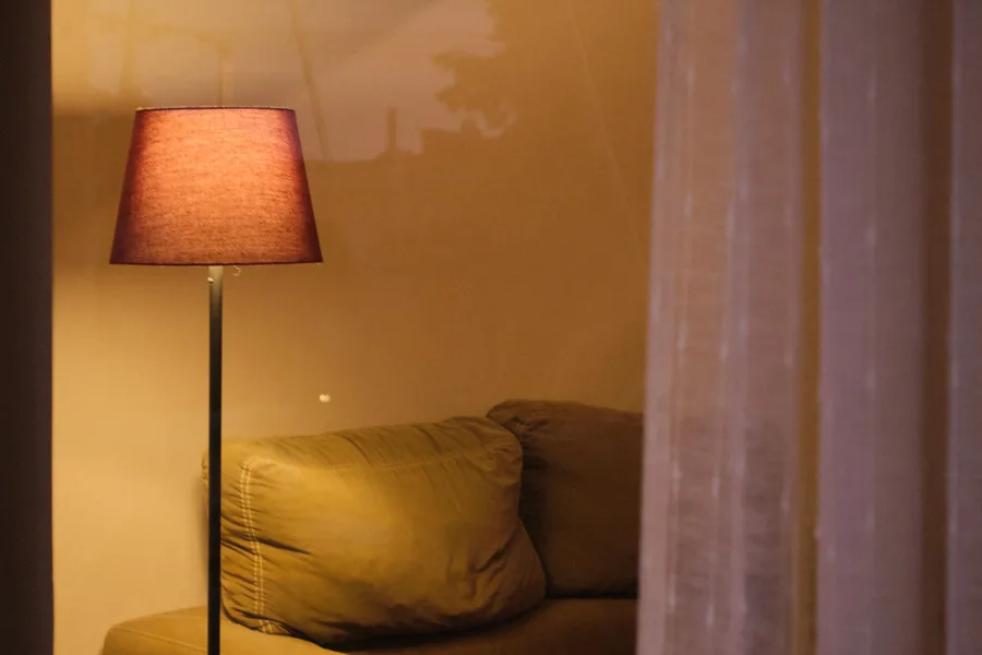 A lit floor lamp beside a sofa in a warmly lit living room in the evening
