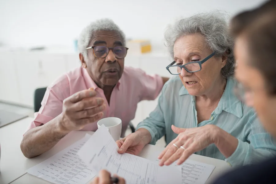 Two older adults at a table going over printed forms with a staff member