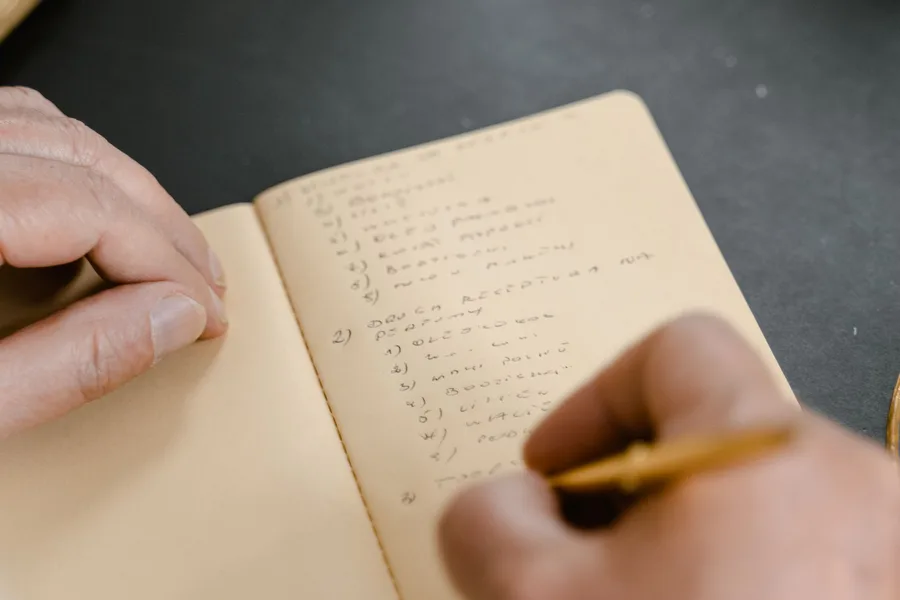 Close-up of a hand writing a numbered list in a small notebook