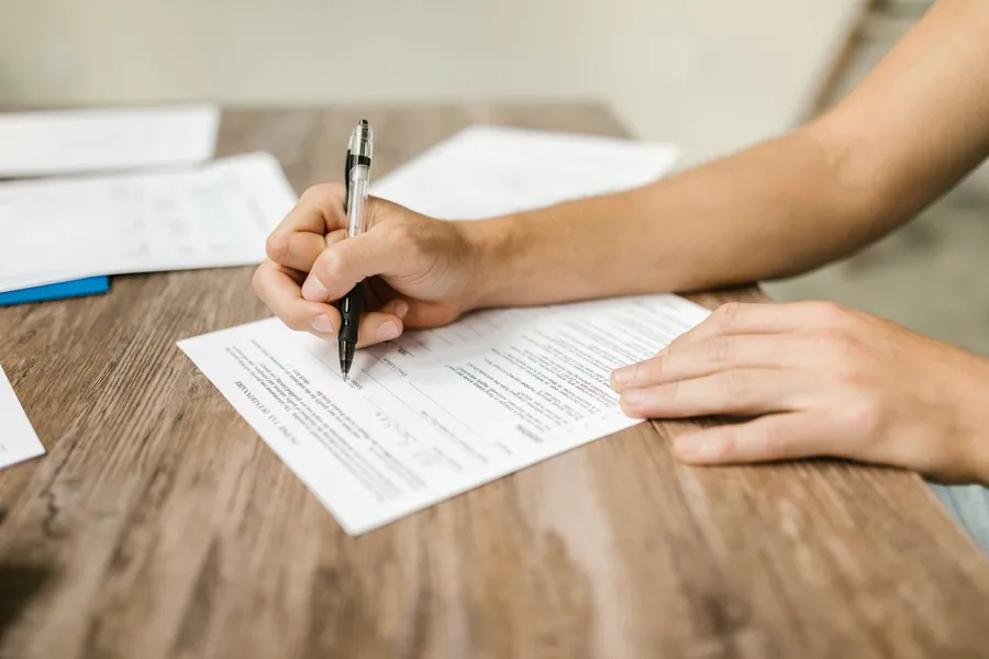 Hands filling out a paper application form at a wooden table