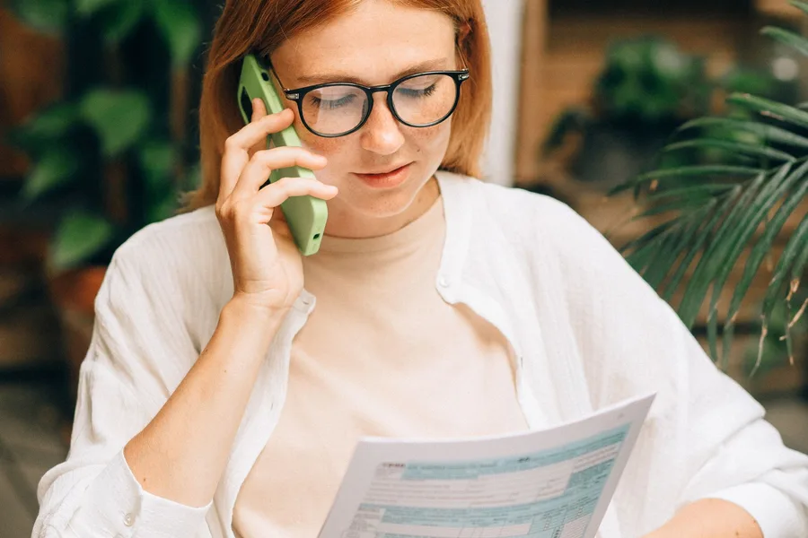 A woman at home on the phone, reading a form as she talks