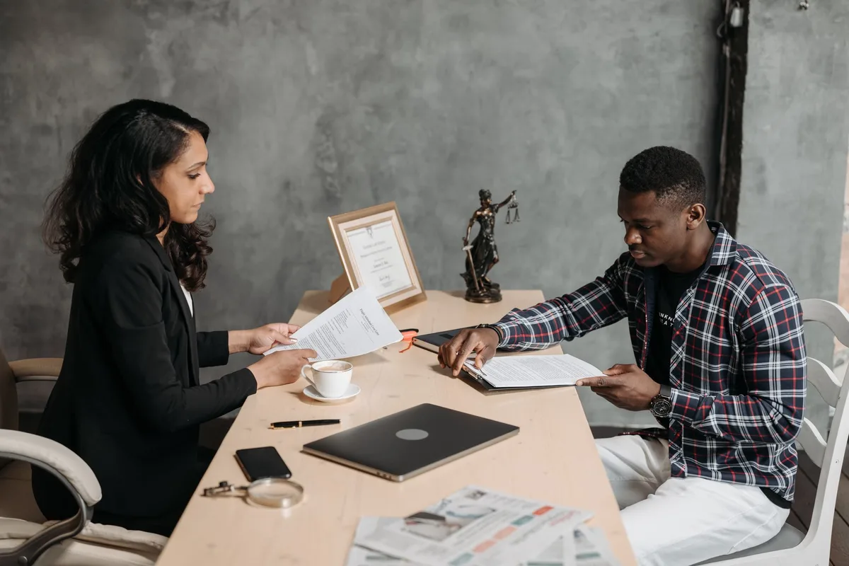 A legal aid advocate and a client sitting across a table, passing documents back and forth