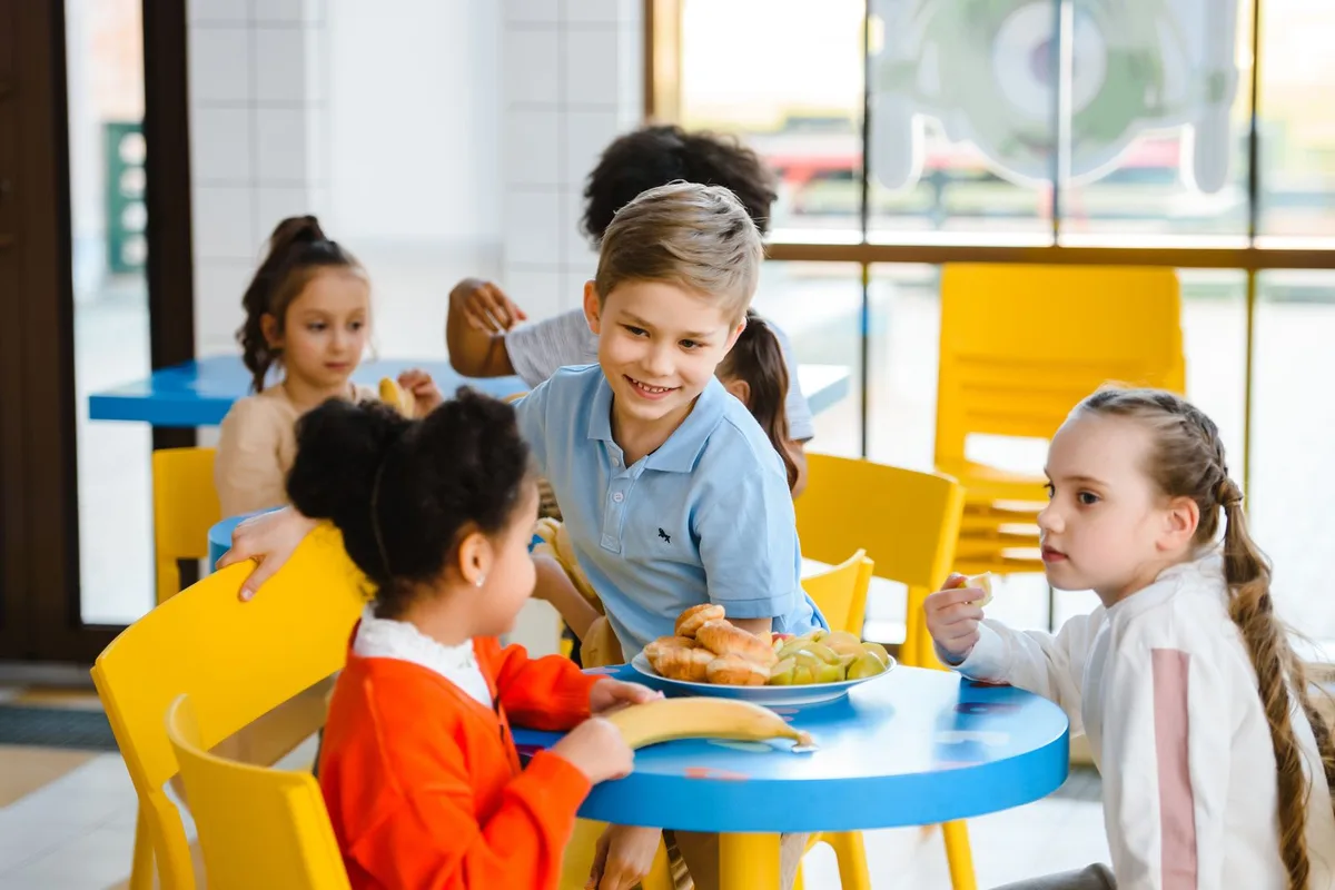 Children sitting together at a table in a bright school cafeteria over lunch