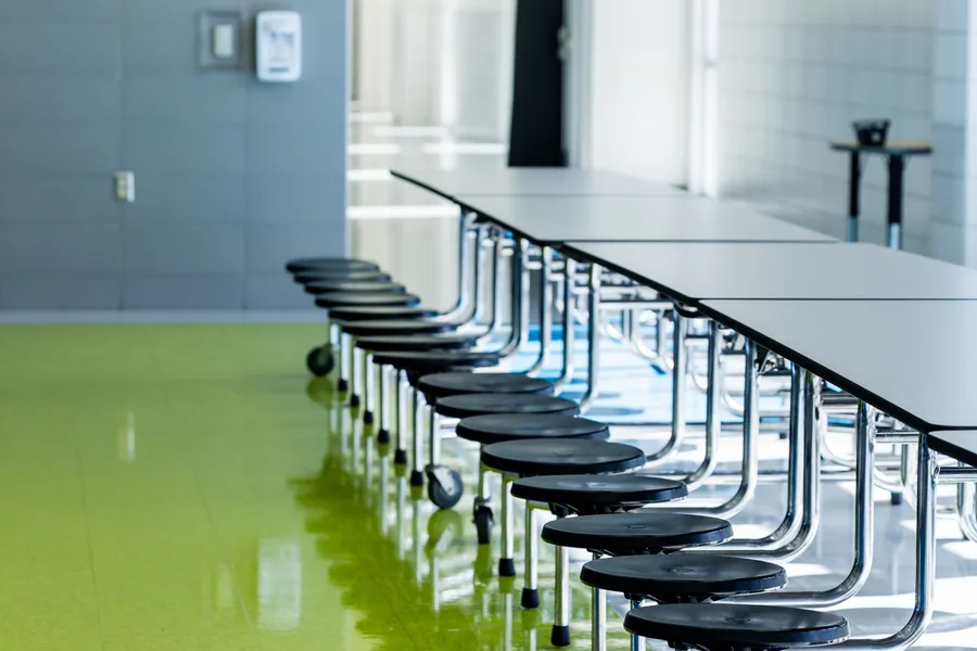 Rows of folding tables and stools in an empty school cafeteria