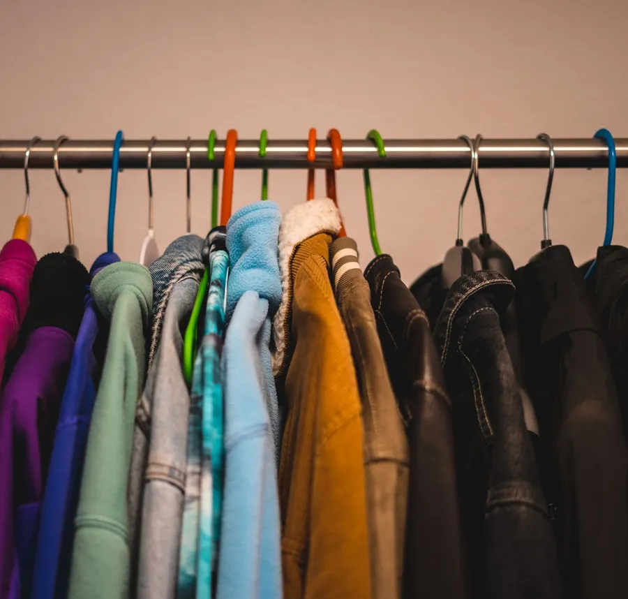 Several colorful jackets and fleeces hang on hangers along a metal clothes rail