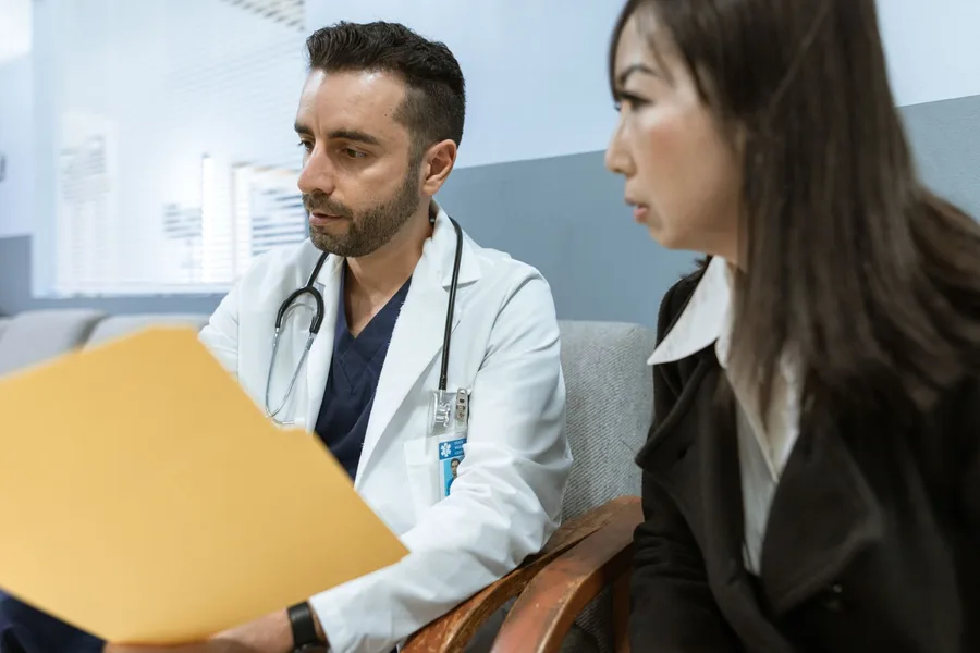 A clinician in a white coat going through a patient file with a patient seated beside him