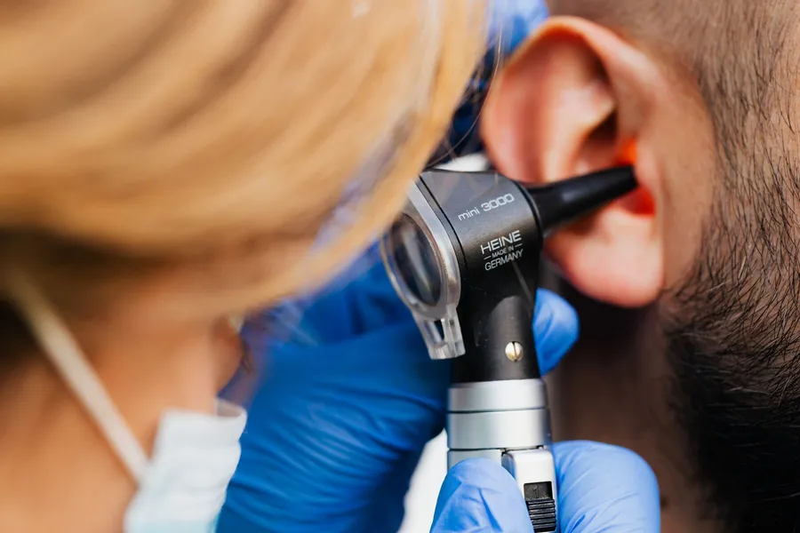 A clinician in gloves examining a patient's ear with a handheld otoscope