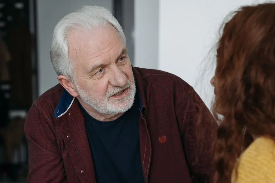 An older man in conversation with a younger woman indoors, talking something through