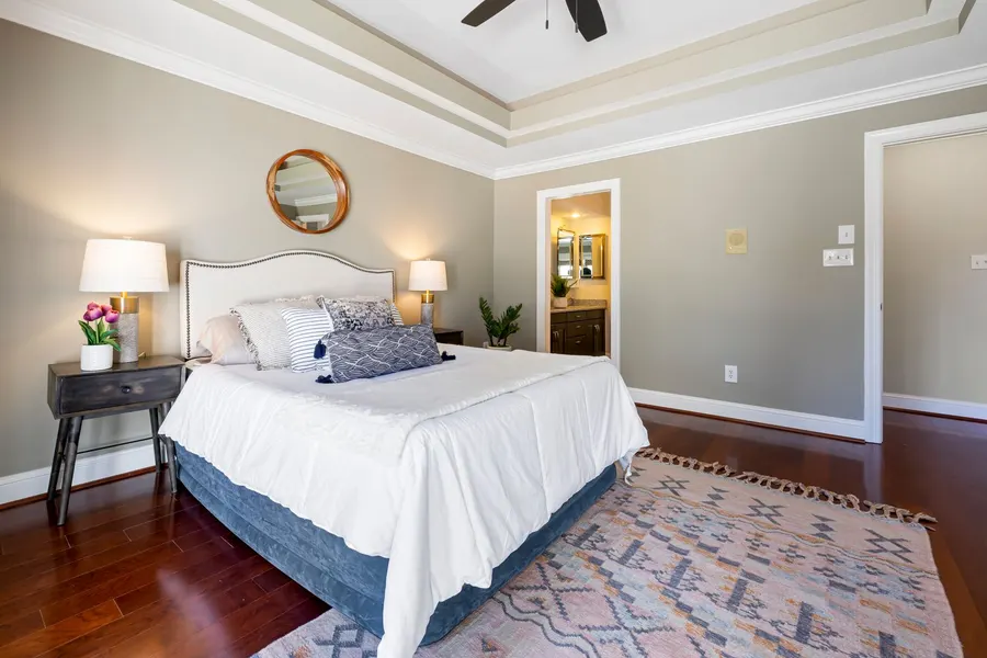A tidy bedroom with a made bed, two bedside lamps, a rug, and an open door to a private bathroom