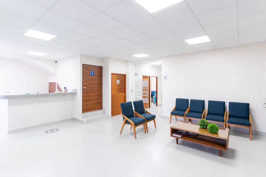 An empty hospital waiting area with a reception counter, chairs and a low table