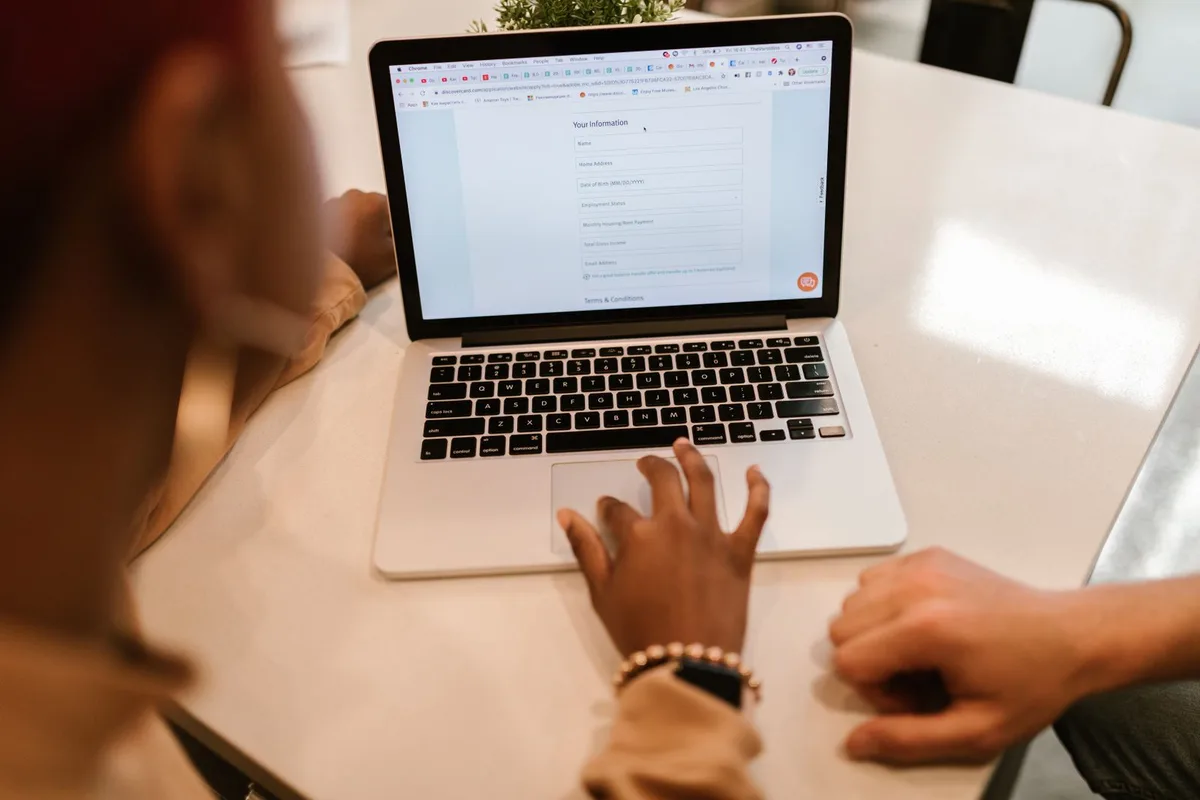 Two people at a table filling out an online form together on a laptop