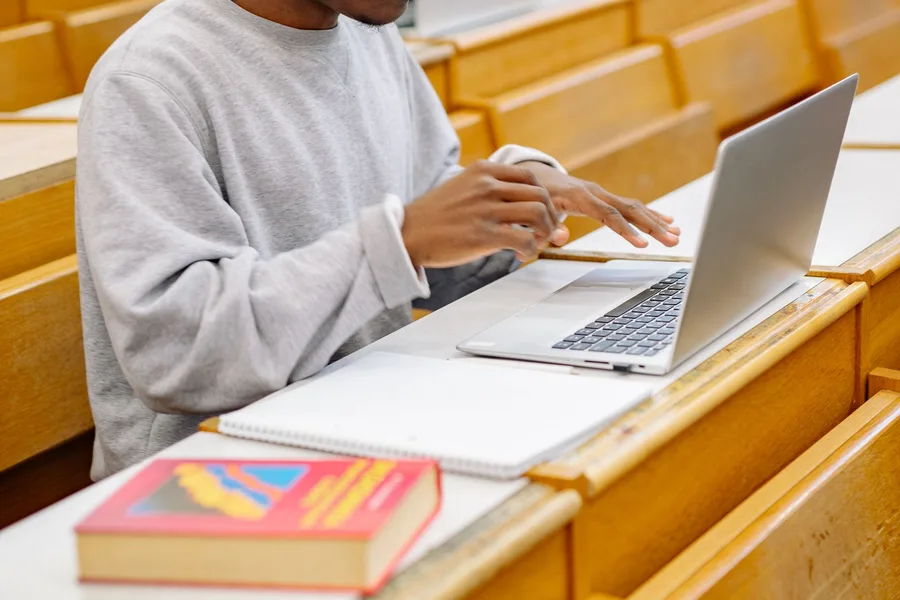A student typing on a laptop at a desk in a university lecture hall