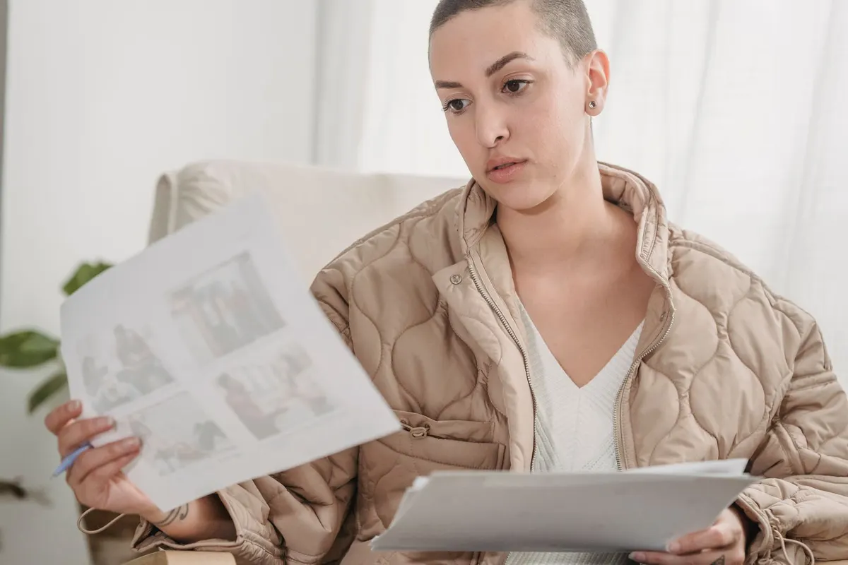 A woman in a quilted jacket sits in a bright room and reads through a page of paperwork