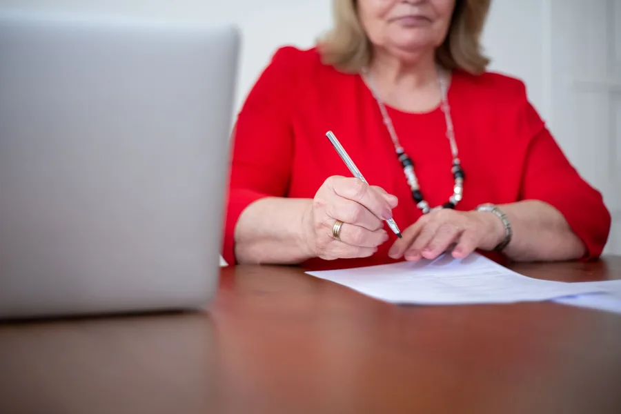 An older woman filling out a printed application form at a desk