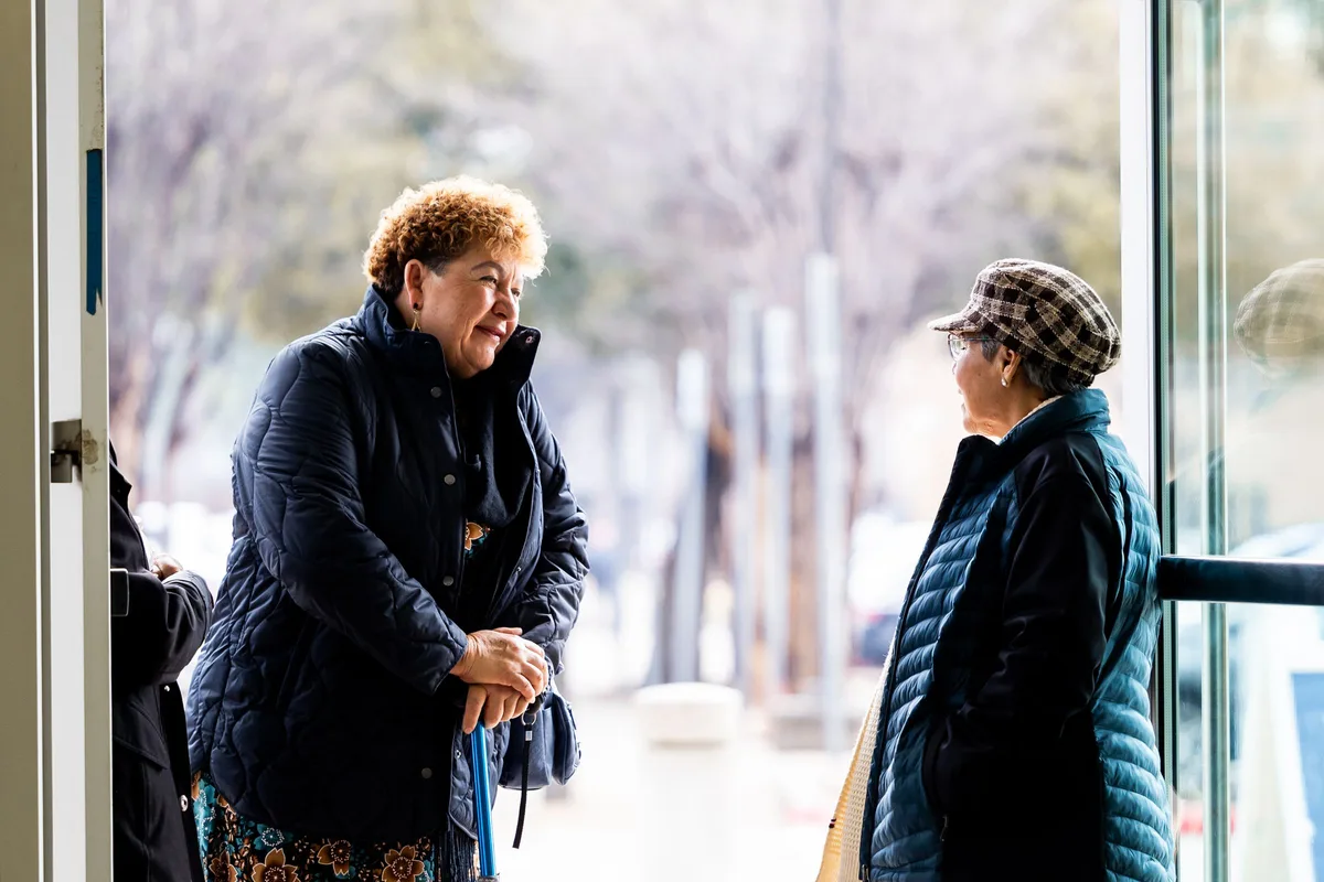 Two older women talking in the doorway of an apartment building on a winter afternoon