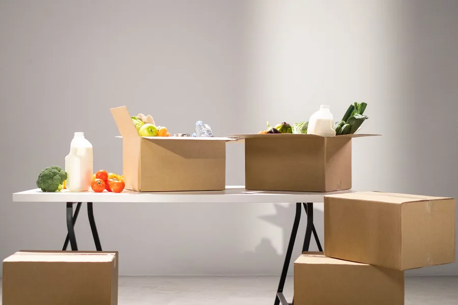 Cardboard boxes packed with fresh produce, milk and staples on a folding table at a food distribution site