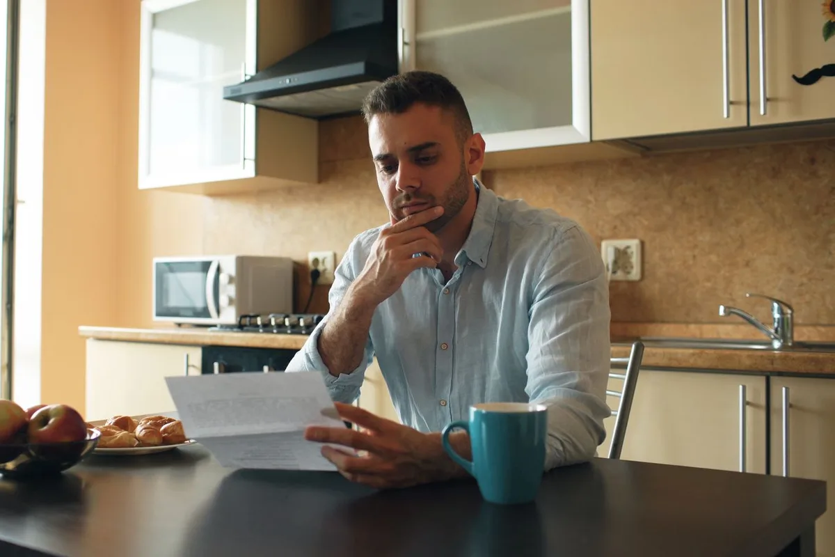 A man sits at his kitchen table reading a letter he has just opened