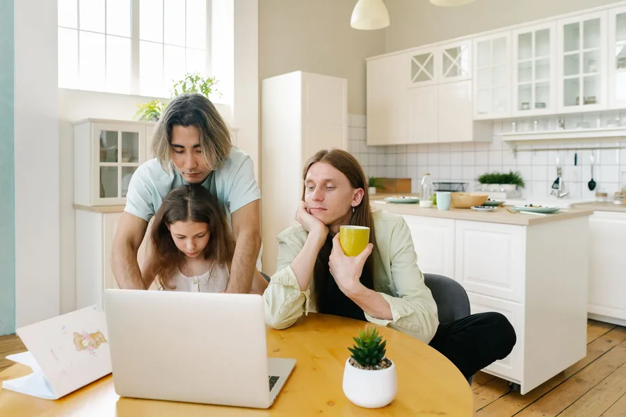 Two parents and a child looking at a laptop together at the kitchen table