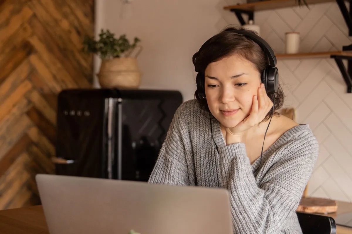 A young woman with headphones using a laptop at the kitchen table