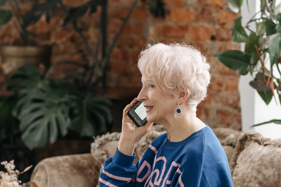 An older woman sitting on her living room couch, talking on a mobile phone