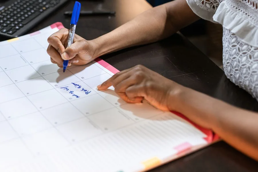 A person marking a date on a large paper desk planner with a pen
