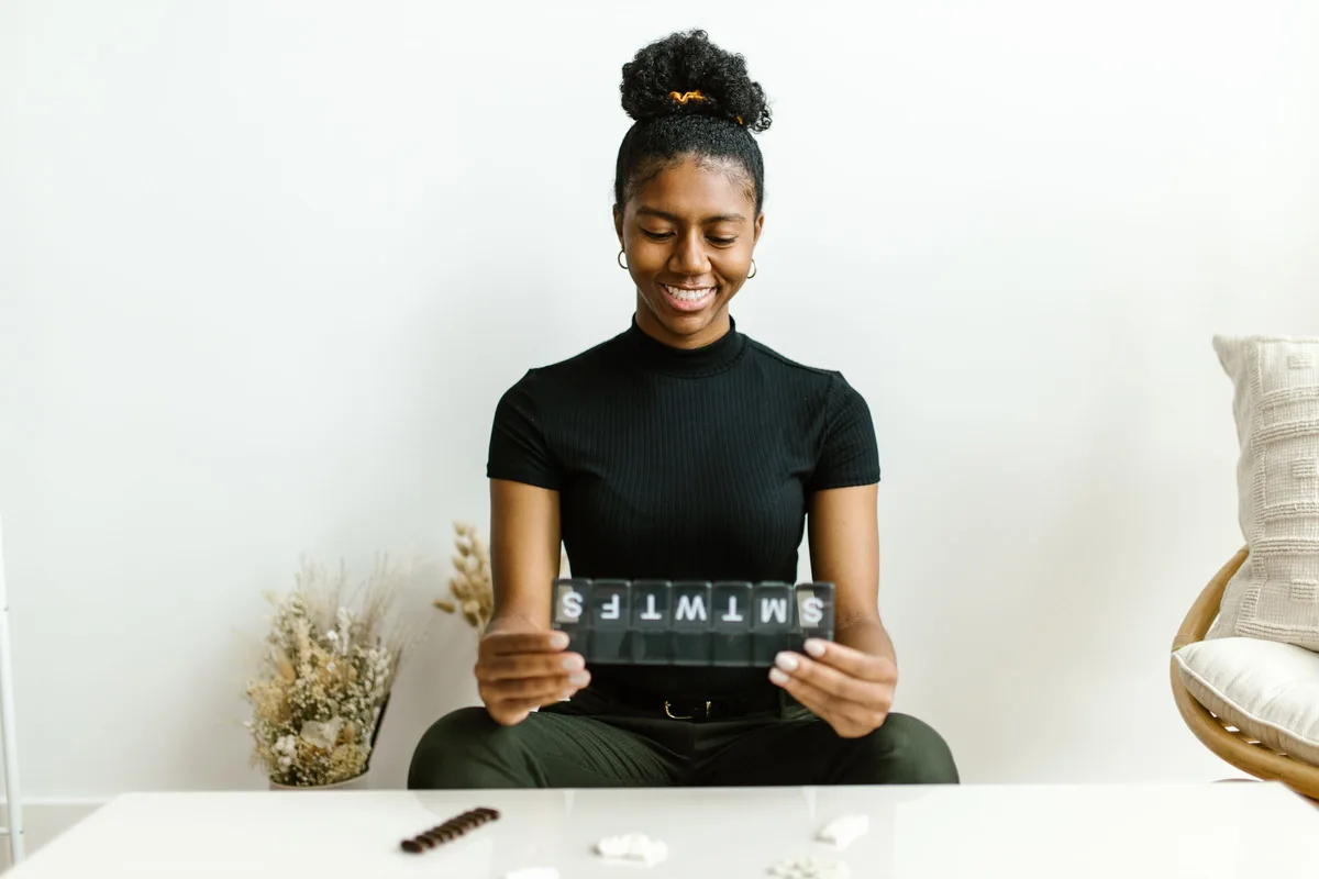 A woman smiling as she holds an open weekly pill organizer labeled with the days of the week