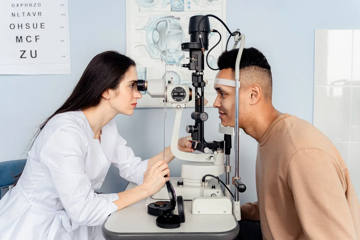 An ophthalmologist examining a patient at a slit lamp, with an eye chart on the clinic wall