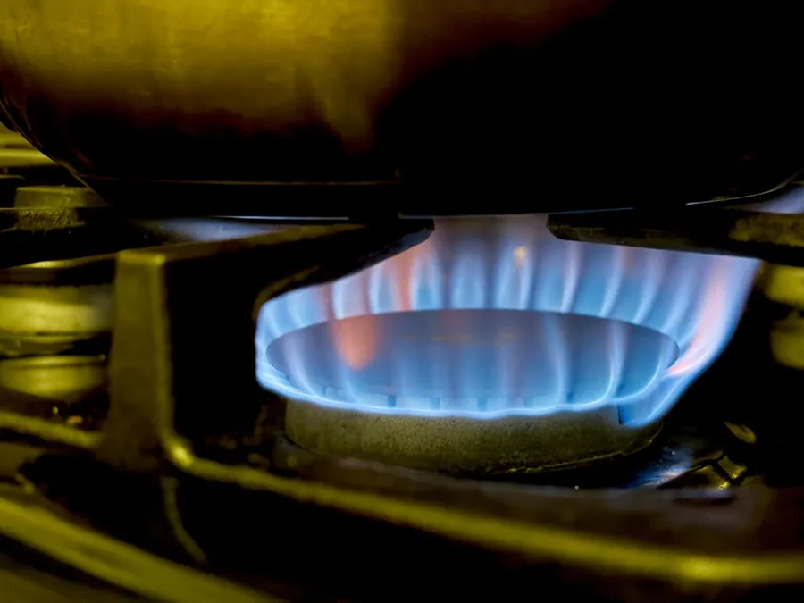 A ring of blue flame burns on a gas stove burner under a pot