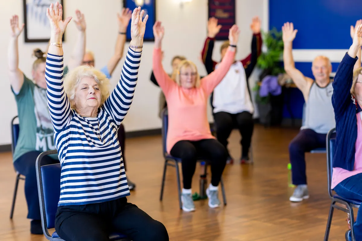 Older adults in a bright activity room taking part in a seated exercise class
