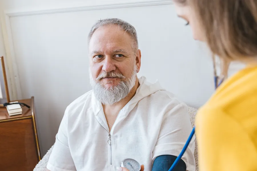 A home health worker checking an older man's blood pressure in his living room