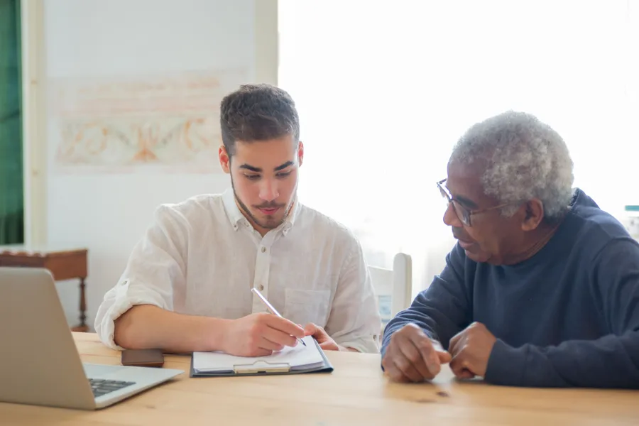 A staff member going through paperwork with an older man at a kitchen table