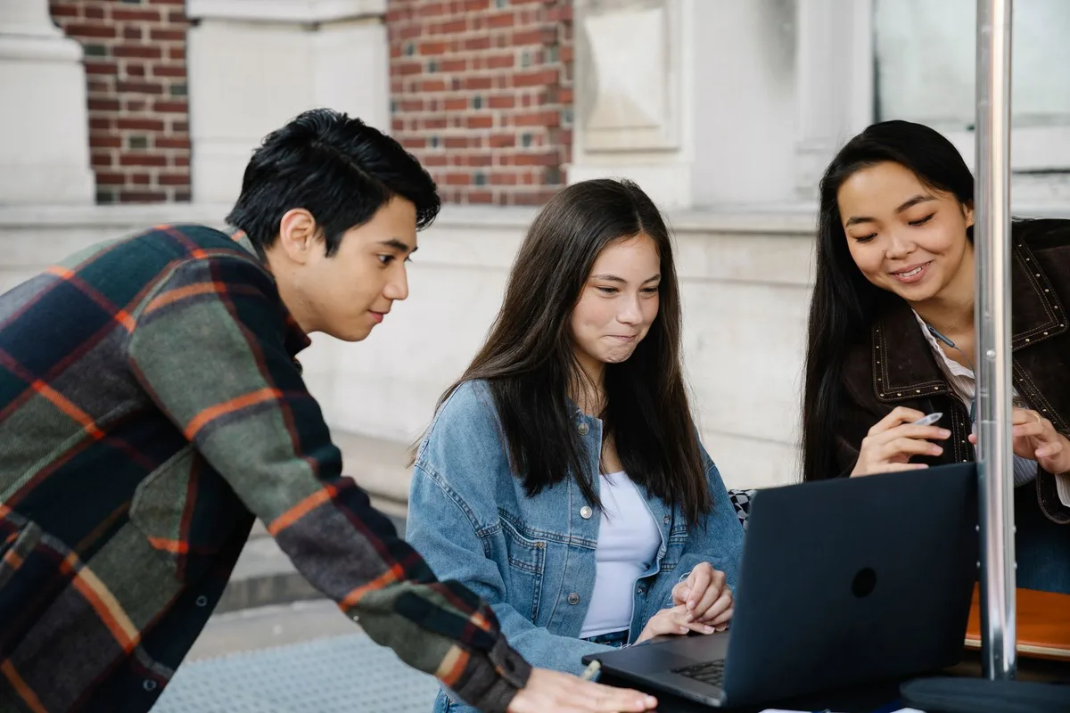 Three college students gathered around a laptop at an outdoor table on campus