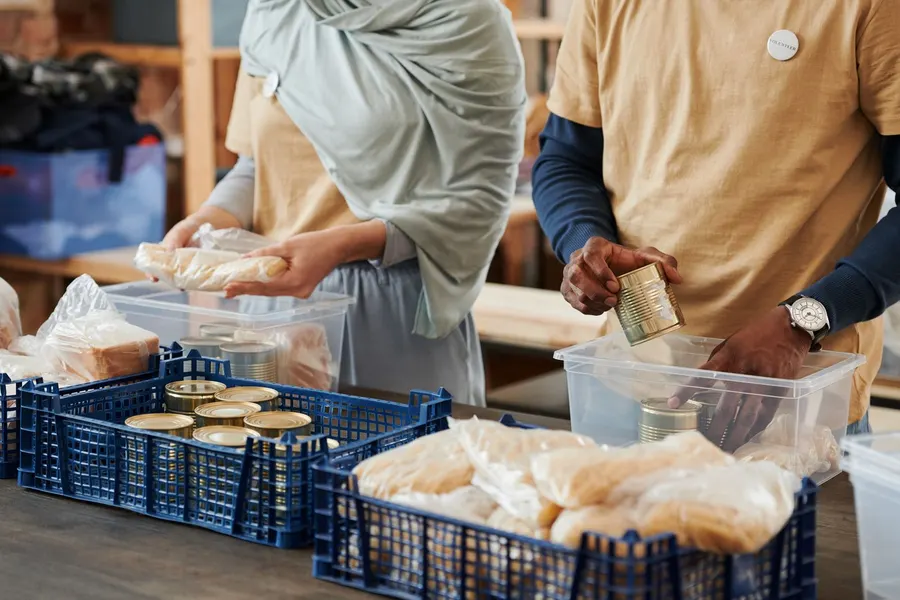 Two volunteers sort donated food and supplies into clear bins and crates on a table
