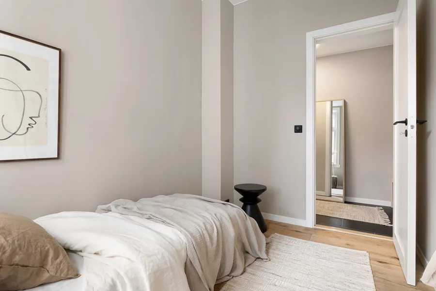 A quiet guest room with a made bed, a side table and a door open to a hallway