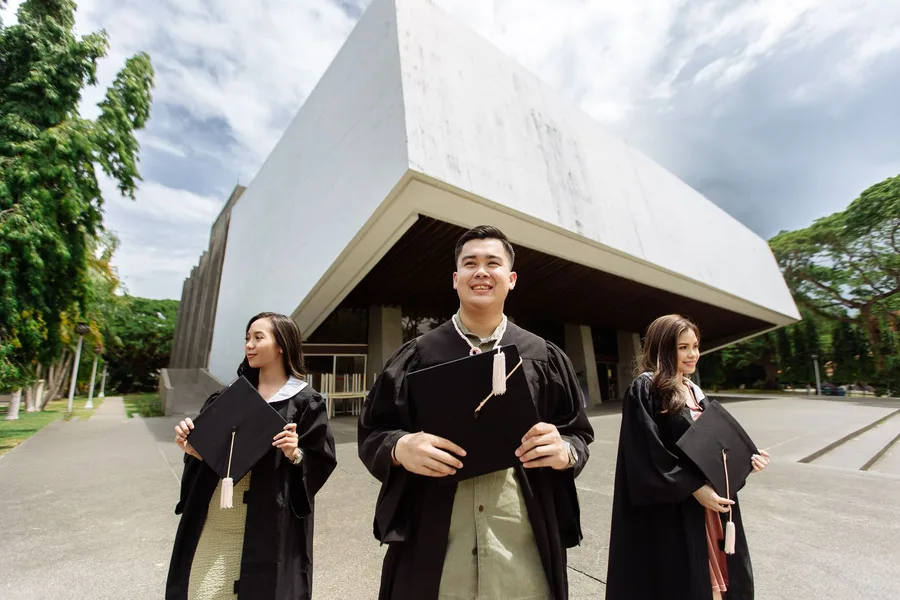 Three graduates in caps and gowns holding rolled diplomas outdoors