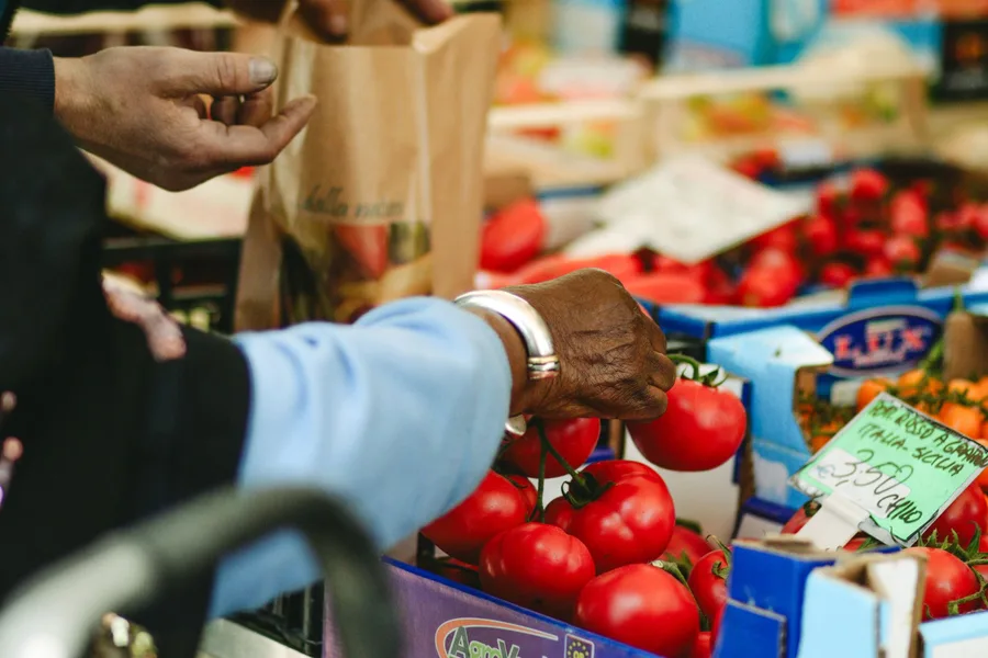 An older person's hands choosing ripe tomatoes from a crate at an outdoor produce market