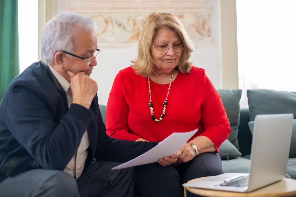An older couple sitting together at home, reading a document with a laptop and a calculator on the table