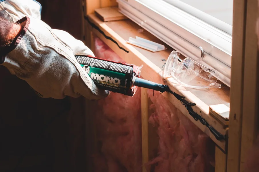 A gloved hand running a bead of sealant along the frame of a window