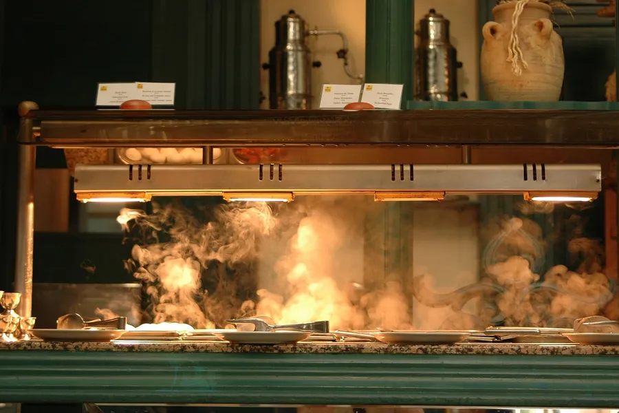 A supermarket hot-food case under heat lamps, steam rising from the trays